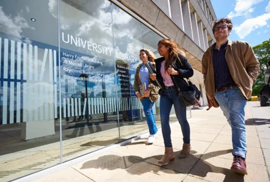 Students walk toward the University library in the sun smiling.